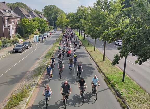 Große Gruppe von Radfahrenden auf einer Straße in Bremen bei Tageslicht. Die Teilnehmenden fahren verschiedene Fahrradtypen und tragen bunte Kleidung.